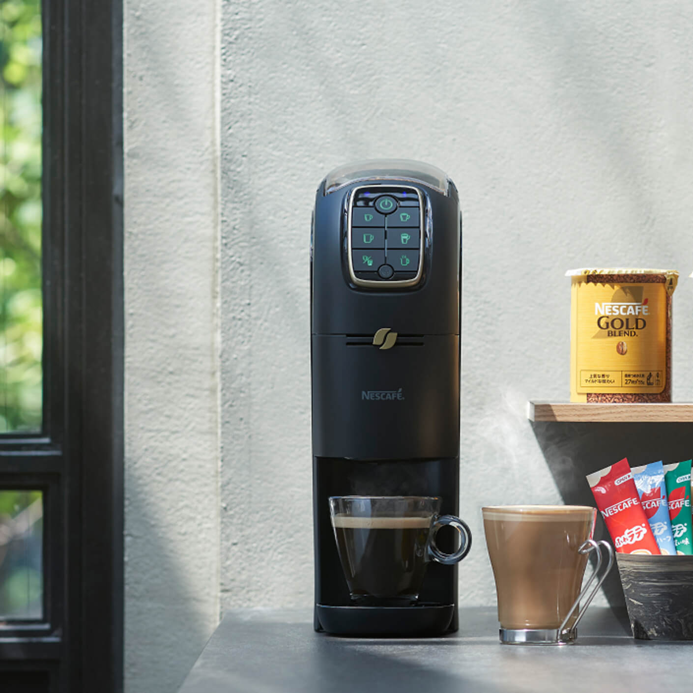 洗練されたネスカフェのコーヒーマシンがコーヒーを一杯淹れており、近くには2つのマグカップとネスカフェ ゴールドブレンドの瓶から湯気が立ち上っています。